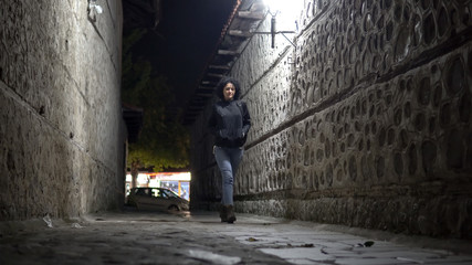 Obraz na płótnie Canvas Woman in jeans and boots walk in Dark Urban Alley at Night, cinematic low angle shot