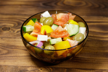 Greek salad in glass bowl on wooden table