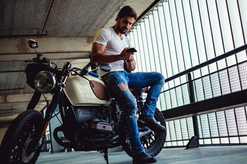 Handsome man sitting on his motorcycle and looking at phone - Powered by Adobe