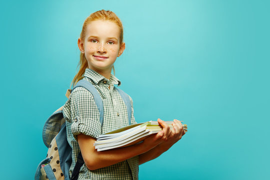Portrait of first-grader schoolchild with backpack and notebooks in hand on isolated blue background. Girl going to school for classes.