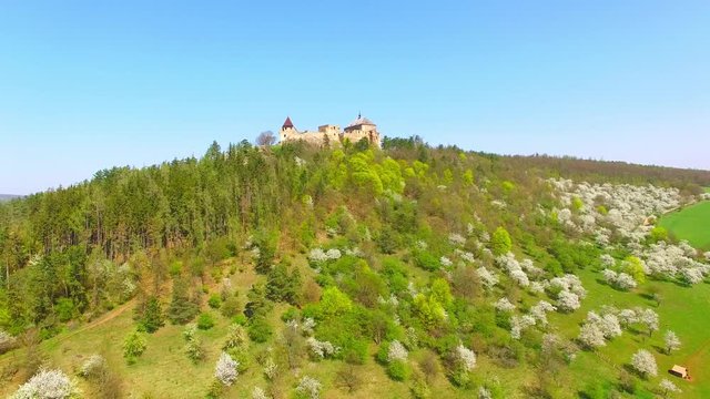 Drone flight around Tocnik Castle in blooming orchard. A royal chateau of Wenceslas IV from the 14th century, adjusted in the Renaissance and the Baroque styles. Famous Czech monument from above. 