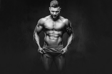 A handsome shirtless tattooed bodybuilder with stylish haircut and beard, wearing sports shorts,...