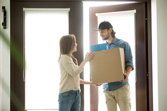 Smiling courier delivering parcel to young woman, happy satisfied customer receiving cardboard box from deliveryman at home, receiver accepting package standing at door, delivery service concept