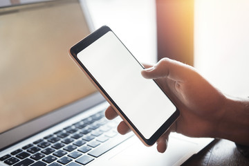 Young man with tattoo holding mobile phone in right hand and working on laptop