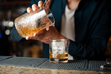 Bartender hands pouring fresh summer alcoholic cocktail into a glass