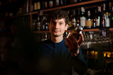 Young curly barman shaking a fresh summer cocktail in a shaker