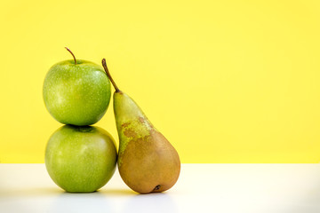 the composition of two fresh green apples and one long pear on yellow background
