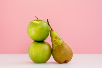 the composition of two fresh green apples and one long pear on pink background
