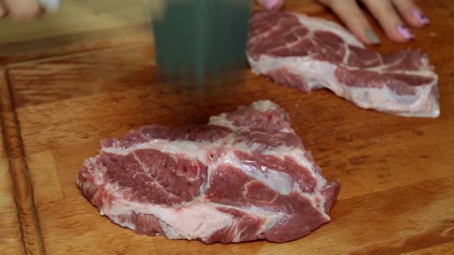 A woman is beating a meat with a hammer, close-up.
