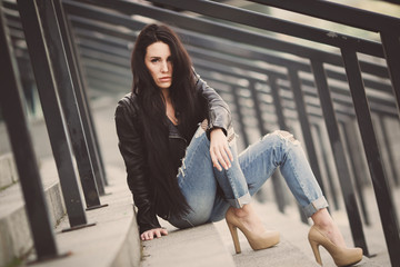 Beautiful fashionable brunette girl sits on the steps in the city. 