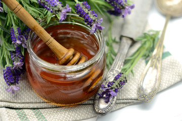 Lavender honey in a glass with flower pot of Lavandula stoechas and antique silverware.