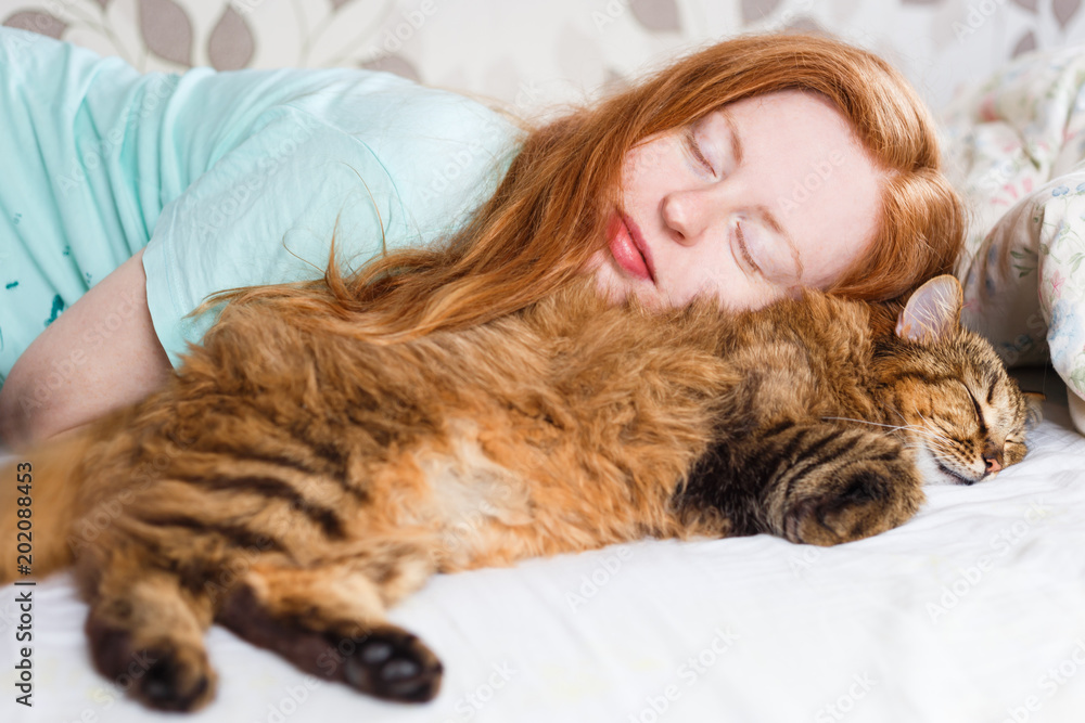 Wall mural young redhair woman sleeping with cat.