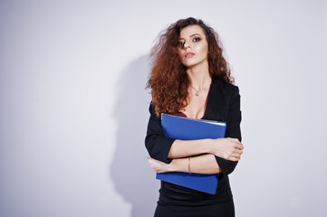 Fototapeta premium Brunette curly haired girl in black office jacket with skirt, on bra with folder of documentts at hands on studio against white background. Sexy businesswoman.