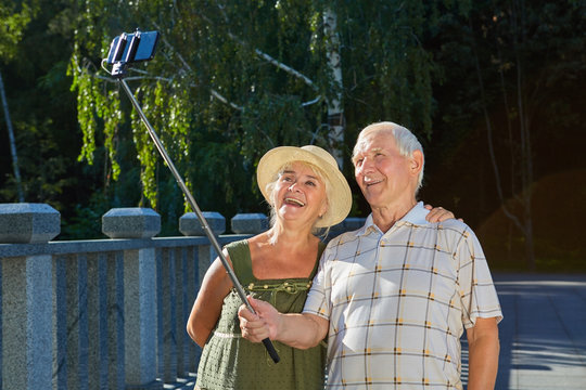 Senior couple taking selfie outdoors. Happy old man holding monopod. Good photography habits.