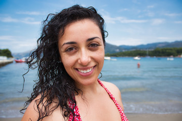 Closeup portrait of a beautiful young smiling woman on a gorgeous beach with blue sea and long hair blowing in the breeze