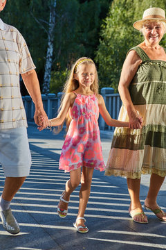 Child holding hands of grandparents. Happy girl outdoors. Info about generations.
