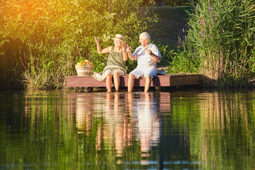 Senior couple sitting near water. People with picnic basket.