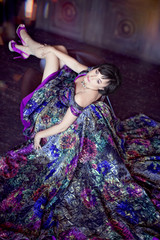 Beautiful woman in luxurious purple dress and violet shoes, sitting in an armchair, throwing her legs up