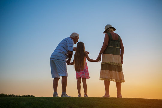 Seniors with grandchild, sunset. Girl and grandparents, evening sky.