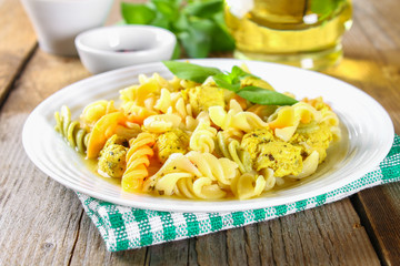 Pasta with slices of fried chicken fillet on an old wooden table.