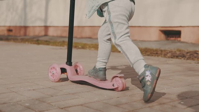 Hapy girl rides on pink scooter outdoor at sunny day in slow motion.