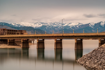 Long exposure of a bridge spanning Lake Chelan with snow-capped mountains in the background