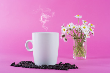 Cup of coffee with smoke and coffee beans and blurred daisy flowers in background in studio