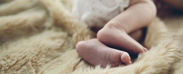 Detail of newborn baby feet lying on a blanket on the bed