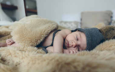 Newborn baby girl with pompom hat sleeping on a blanket