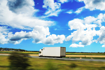 Box truck driving fast on the countryside road against blue sky with clouds