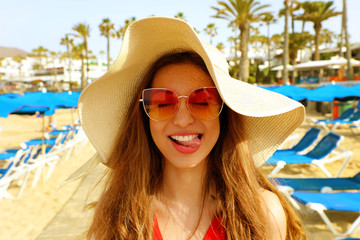 Portrait of beautiful blonde woman with straw hat and sunglasses having fun at beach. Funny...