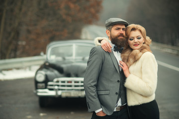 brutal bearded man with a smart mustache brunette embrace woman at car retro style.