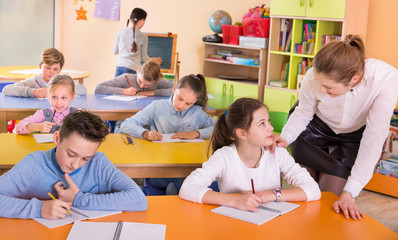 Teacher woman helping children during lesson in schoolroom