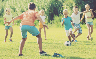 Obraz na płótnie Canvas Group of friendly kids playing football together on green lawn i