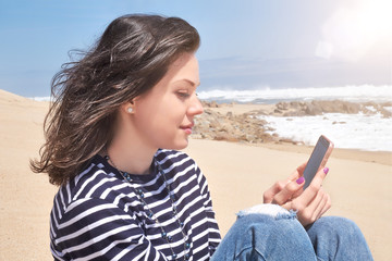 Fototapeta na wymiar Smiling woman in a striped T-shirt with smartphone relaxing on beach, summer day