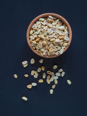 Roasted peanuts in wooden bowl on a dark background. The view from the top.