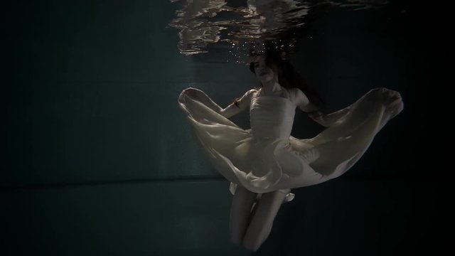 Young pretty woman is swimming in aquarium underwater. She is rising head over surface for breathing, her body is floating, view from bottom