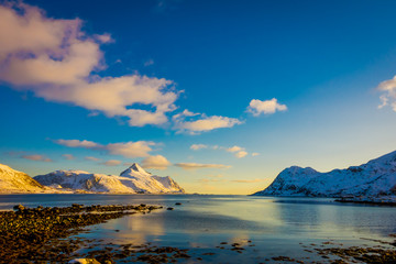 Sunset at Henningsvaer shoreline with huge mountains covered with snow in a gorgeous blue sky on Lofoten Islands, Austvagoya