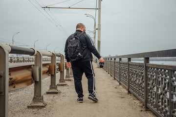 Tourist photographer with camera and backpack  is walking along bridge. Rear view. 