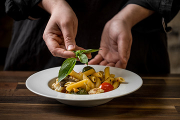 Close-up on the hand of a chef placing a basil leaf in a plate penne.