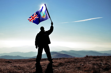 Successful silhouette man winner waving Montserrat flag on top of the mountain peak