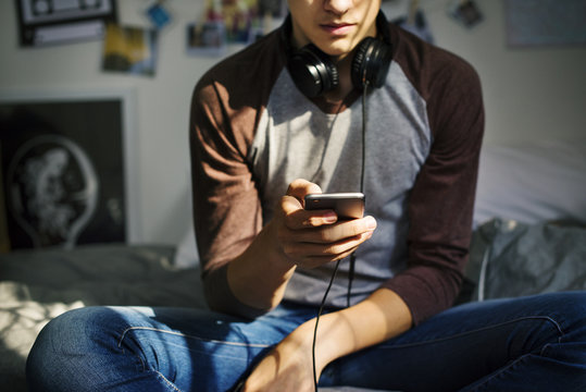 Teenage boy in a bedroom listening to music through his smartphone