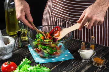 Man preparing salad with fresh vegetables on a wooden table. Cooking tasty and healthy food