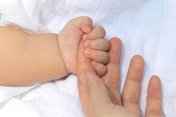 Baby uses his small fingers to hold his mother's finger to make him feel love, warm and secure while he is sleeping