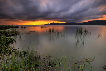 Tropical lake with dramatic sky and clouds during sunset.