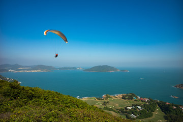 Tandem paragliders having fun paragliding over Dragon's Back hiking trail in Hong Kong, Asia