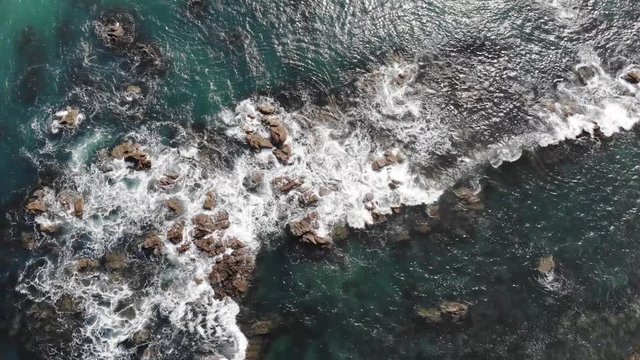 Aerial shot looking down on waves crashing onto rocks in New Zealand