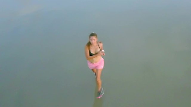 Aerial panning with drone on attractive and sexy Asian sport runner woman in running workout practice at sunset beach backlit as silhouette in fitness and healthy lifestyle concept