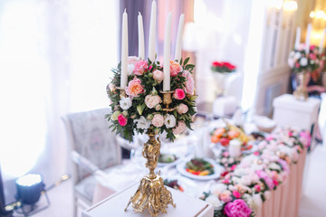 White candles on metal gold chandelier stand on tables at luxury wedding reception in restaurant. stylish decor and adorning