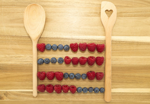 Vintage abacus calculator frame made of kitchen spoons, fresh blueberries and raspberries on a brown wooden cutting board